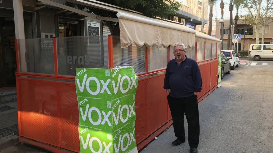 José Antonio Herrera posa junto a los carteles de VOX pegados en la terraza del bar que regenta junto a su socia, de nacionalidad búlgara.