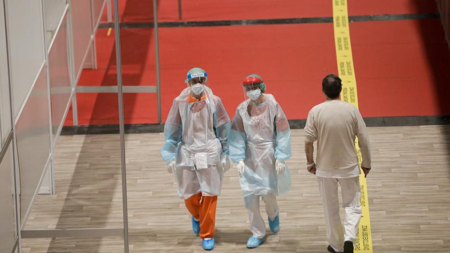 Trabajadores sanitarios protegidos caminan por el interior del hospital de campaña montado en IFEMA. 