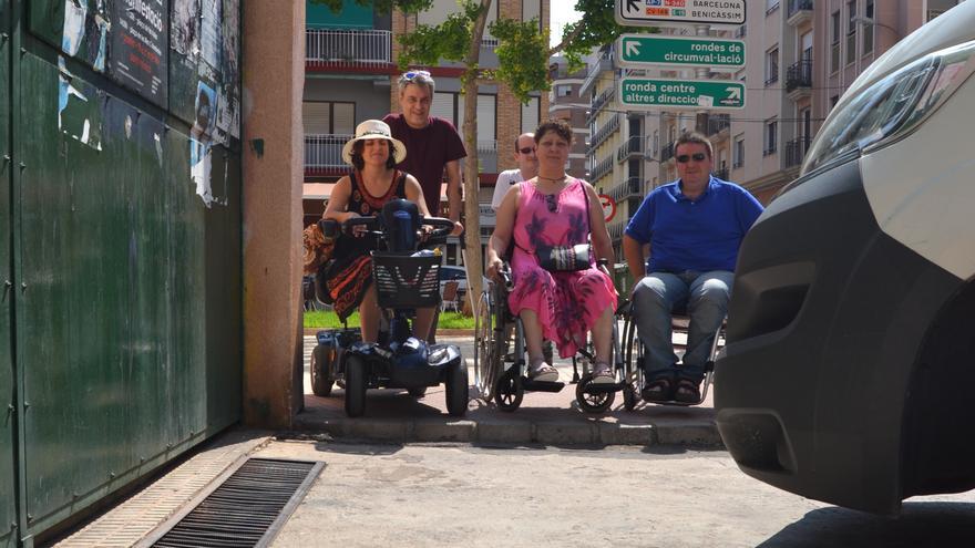 Miembros de la Plataforma Castelló Vida Independiente posan junto a un escalón y una acera invadida por coches, dos de las "trampas" habituales en su movilidad diaria por la ciudad. 