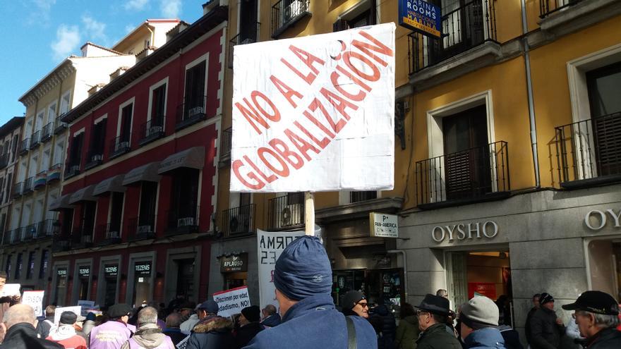 Un hombre sostiene una pancarta con el mensaje "No a la globalización" en la manifestación de pensionistas, taxistas y afectados por la hipoteca en Madrid.