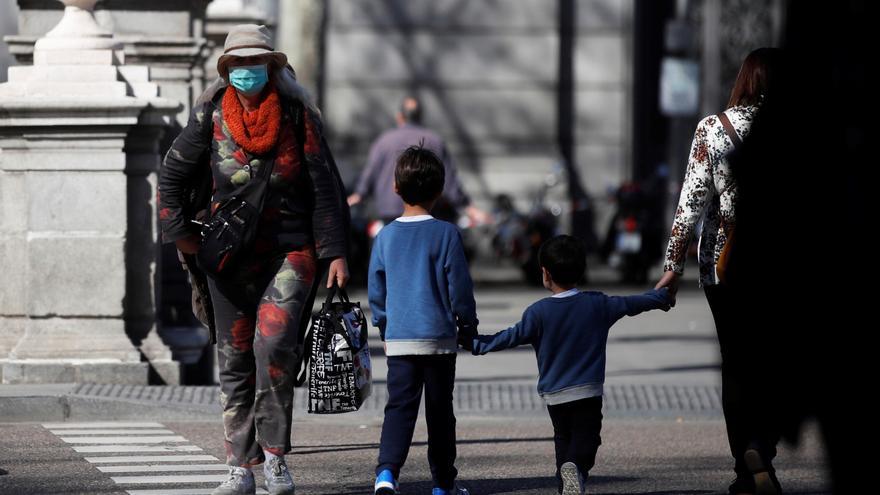 Una mujer con mascarilla se cruza con una familia en un paso de cebra de Madrid.