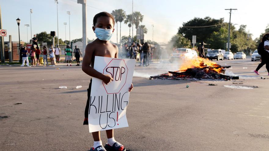 Protegido con mascarilla, un niño sujeta una pancarta en una calle cortada durante las protestas en Tampa, Florida
